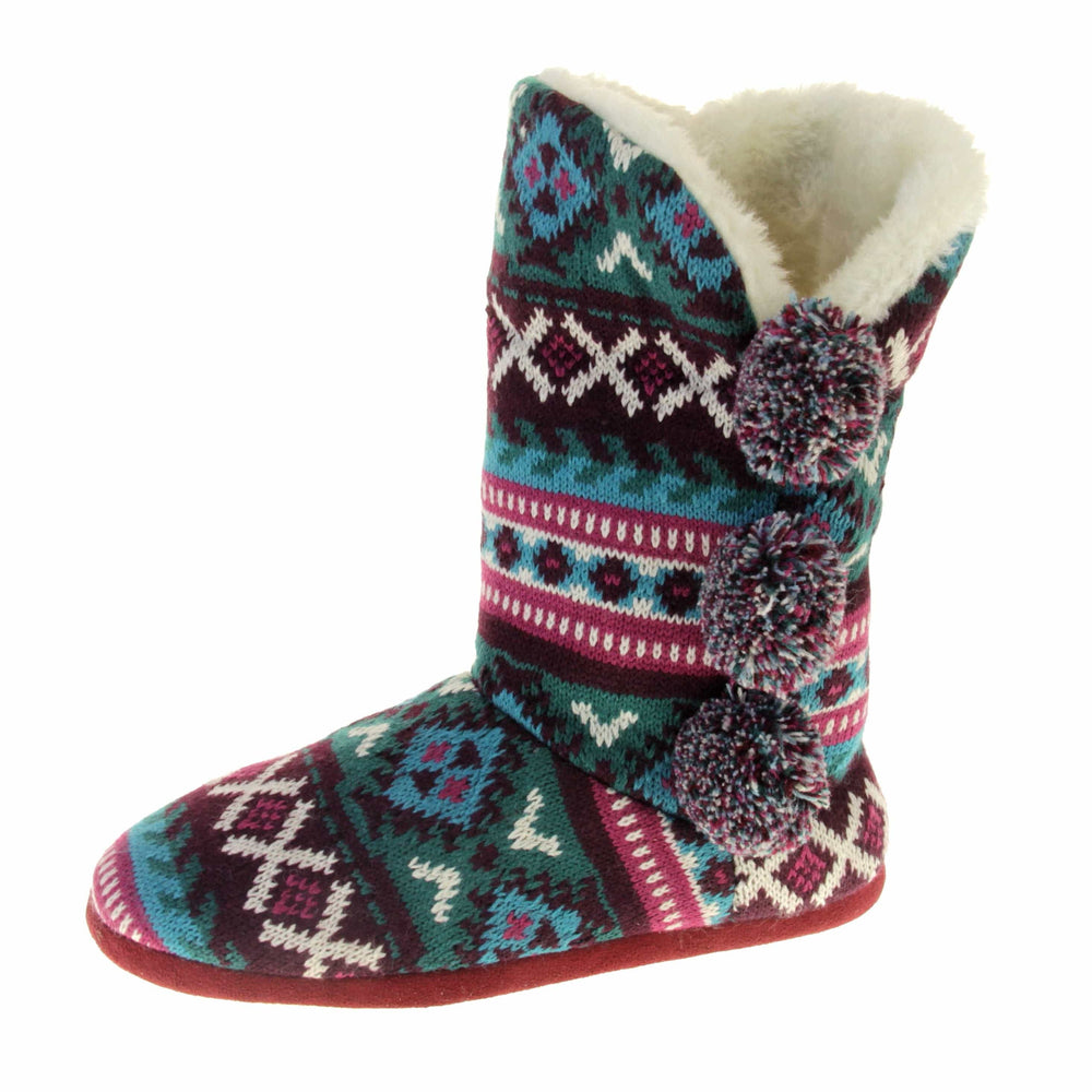 Cable knit slipper boots. Multi coloured patterned knit upper in Aztec style with pom poms to the side, light beige plush faux fur trim and lining. Left foot taken at angle.