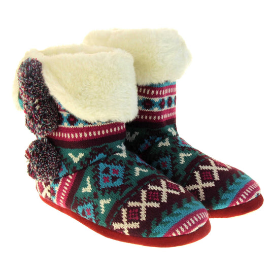 Cable knit slipper boots. Multi coloured patterned knit upper in Aztec style with pom poms to the side, light beige plush faux fur trim and lining. Both feet together at angle.