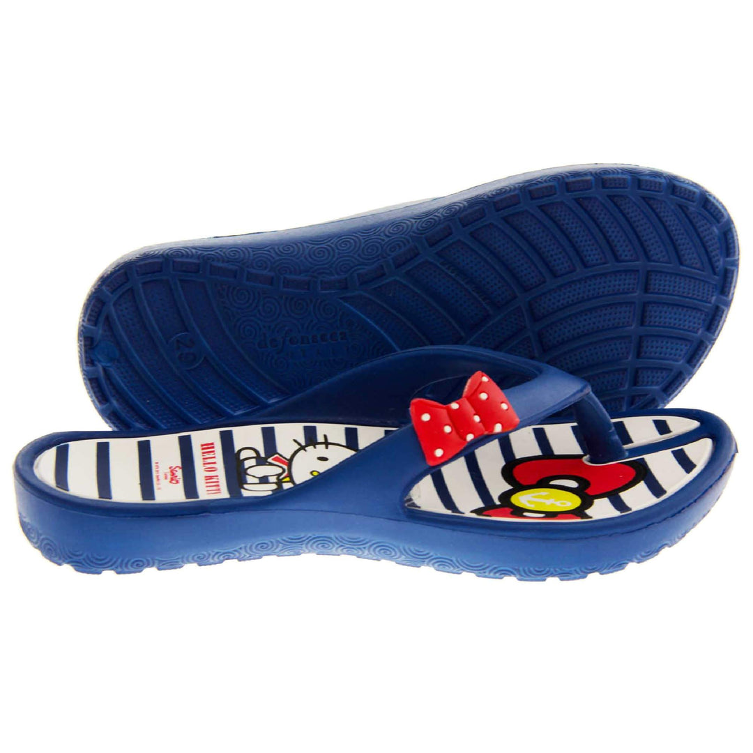 Children's flip flop. Hello Kitty flip flop with navy blue sole and straps in a toe-post design with small red bow with white spots on. White and navy striped insole with Hello Kitty design on. Both shoes from a size profile with the left foot on its side to show the sole.