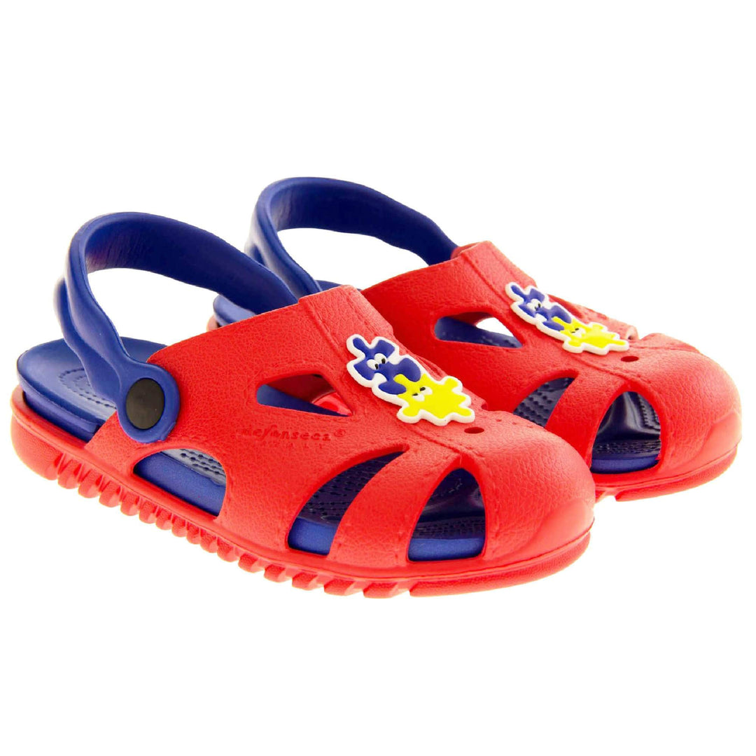 Childrens summers sandals. Fisherman style synthetic sandals with red upper and outer sole. Blue ankle strap and insole. Blue and yellow jigsaw detail to the centre of the upper. Both shoes next to each other at a slight angle.