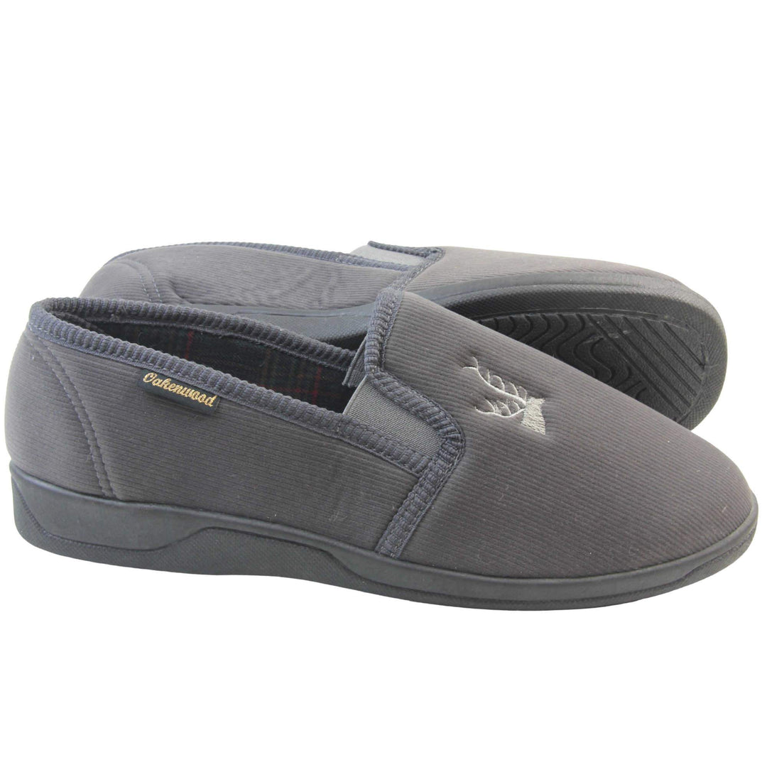 Classic Slippers. Mens full back slippers with a grey velour uppers. Grey elasticated panels joining the tongue to the top of the slippers. Grey stag head detail embroidered onto the top of the upper, near the tongue. Small black label on the outside rim, with Oakenwood branding sewn in gold. Plaid textile lining. Both feet from side profile with left foot on its side to show the sole.