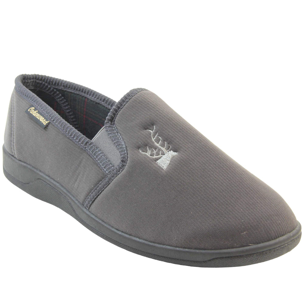 Classic Slippers. Mens full back slippers with a grey velour uppers. Grey elasticated panels joining the tongue to the top of the slippers. Grey stag head detail embroidered onto the top of the upper, near the tongue. Small black label on the outside rim, with Oakenwood branding sewn in gold. Plaid textile lining. Right foot at an angle.