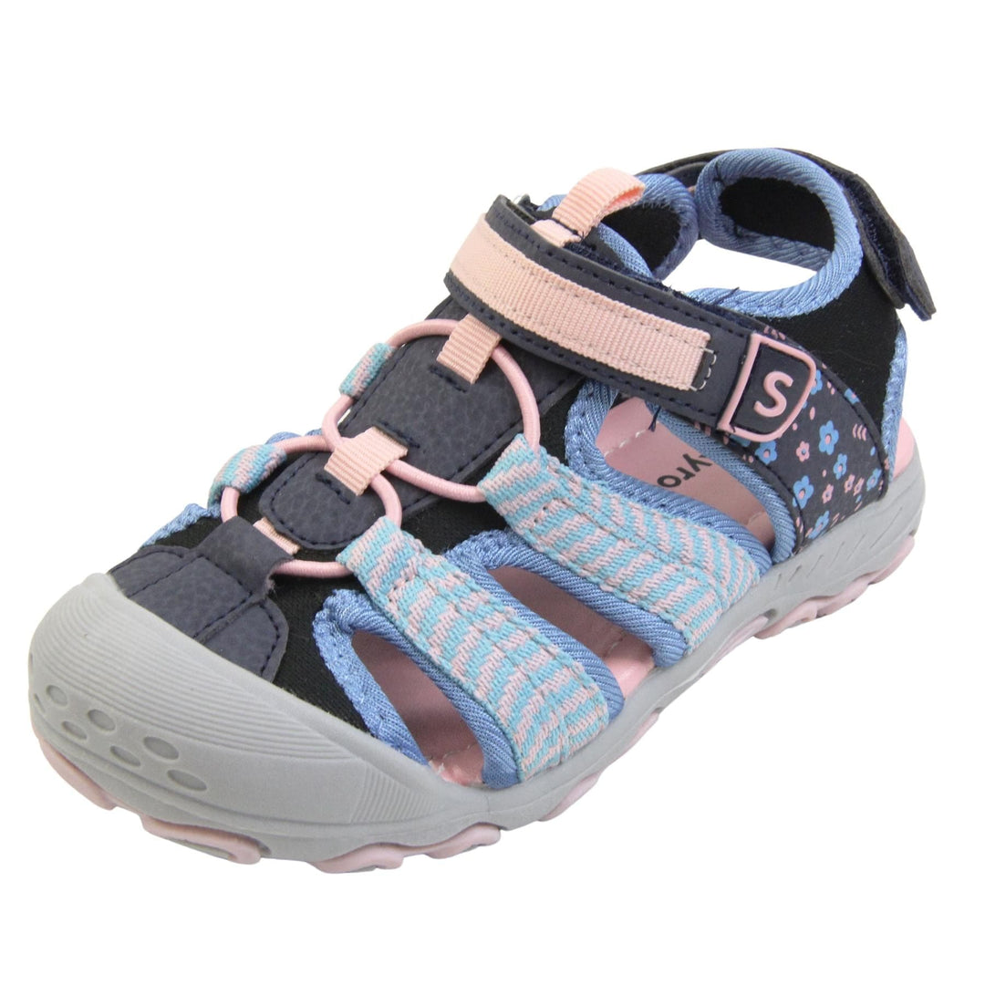 Closed toe girls sandals. Strappy beach sandals with navy mesh and faux leather uppers. With baby blue and pink textile strap detailing. Pink elasticated faux laces to the front. Navy faux leather straps around the front and back of the ankle with touch fastening. Pink and blue flower print detail to the heel sides. Pink insole and grey rubbery outsole and toe bumper with grey and pink grip on the bottom. Left foot at an angle.
