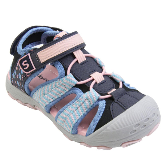 Closed toe girls sandals. Strappy beach sandals with navy mesh and faux leather uppers. With baby blue and pink textile strap detailing. Pink elasticated faux laces to the front. Navy faux leather straps around the front and back of the ankle with touch fastening. Pink and blue flower print detail to the heel sides. Pink insole and grey rubbery outsole and toe bumper with grey and pink grip on the bottom. Right foot at an angle.
