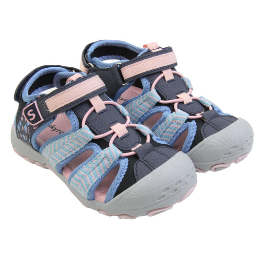 Closed toe girls sandals. Strappy beach sandals with navy mesh and faux leather uppers. With baby blue and pink textile strap detailing. Pink elasticated faux laces to the front. Navy faux leather straps around the front and back of the ankle with touch fastening. Pink and blue flower print detail to the heel sides. Pink insole and grey rubbery outsole and toe bumper with grey and pink grip on the bottom. Both feet together at an angle.