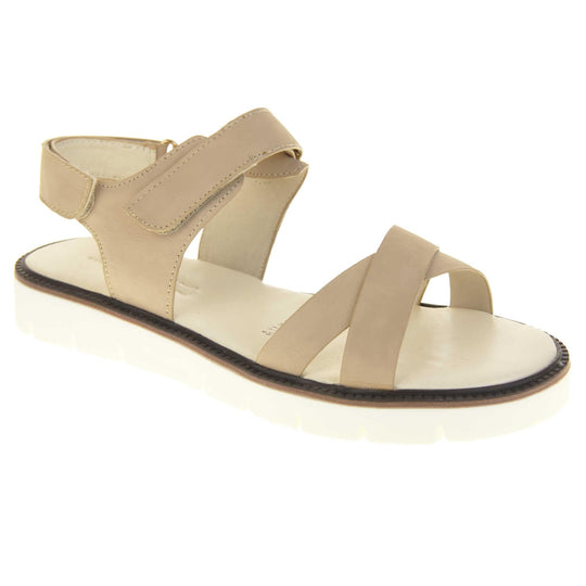 Comfortable flat sandals. Classic womens strappy sandals with beige faux leather straps around the ankle and dual straps crossed over the toes. The ankle strap has a touch fastening at the ankle and the heel. Beige faux leather cushioned insoles. Small white platform outsole with a black rim around the top. Right foot at an angle.