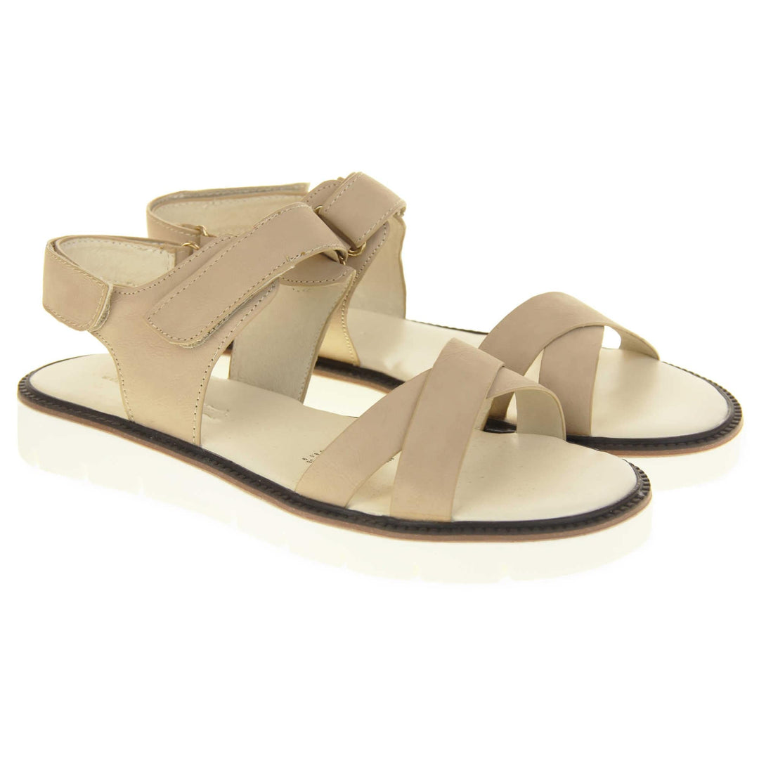 Comfortable flat sandals. Classic womens strappy sandals with beige faux leather straps around the ankle and dual straps crossed over the toes. The ankle strap has a touch fastening at the ankle and the heel. Beige faux leather cushioned insoles. Small white platform outsole with a black rim around the top. Both shoes together from an angle