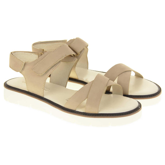 Comfortable flat sandals. Classic womens strappy sandals with beige faux leather straps around the ankle and dual straps crossed over the toes. The ankle strap has a touch fastening at the ankle and the heel. Beige faux leather cushioned insoles. Small white platform outsole with a black rim around the top. Both shoes together from an angle