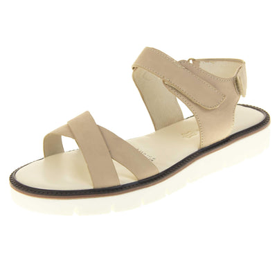 Comfortable flat sandals. Classic womens strappy sandals with beige faux leather straps around the ankle and dual straps crossed over the toes. The ankle strap has a touch fastening at the ankle and the heel. Beige faux leather cushioned insoles. Small white platform outsole with a black rim around the top. Left foot at an angle.
