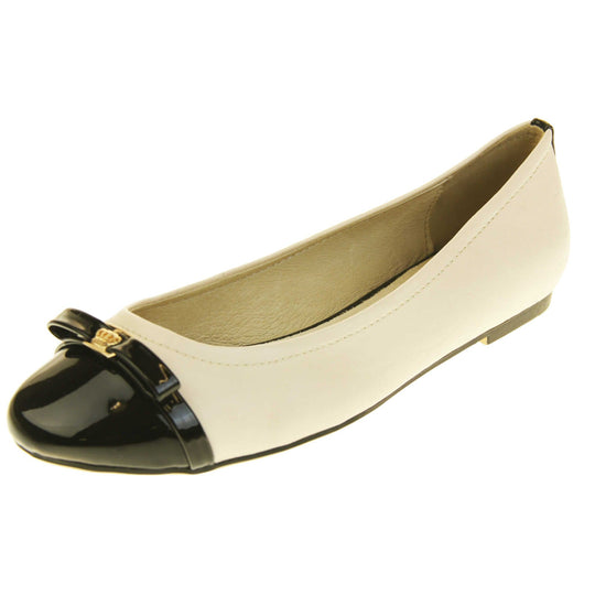 Cream dolly shoes. Cream leather ballet pumps with black patent toe and bow detail. Black stripe down the heel of the upper. Beige outsole with black rim and with a very slight heel. Left foot at an angle.