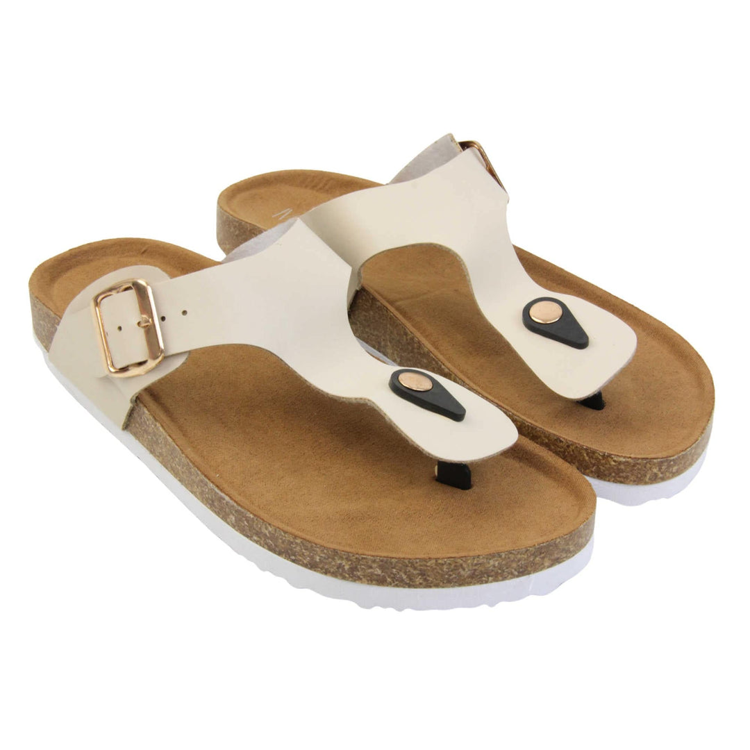 Cream flip flops. Cream faux leather strap with toe post to the front and gold buckle to the outside. Soft tan faux suede footbed with cork effect outsole and white sole. Both feet together at a slight angle.