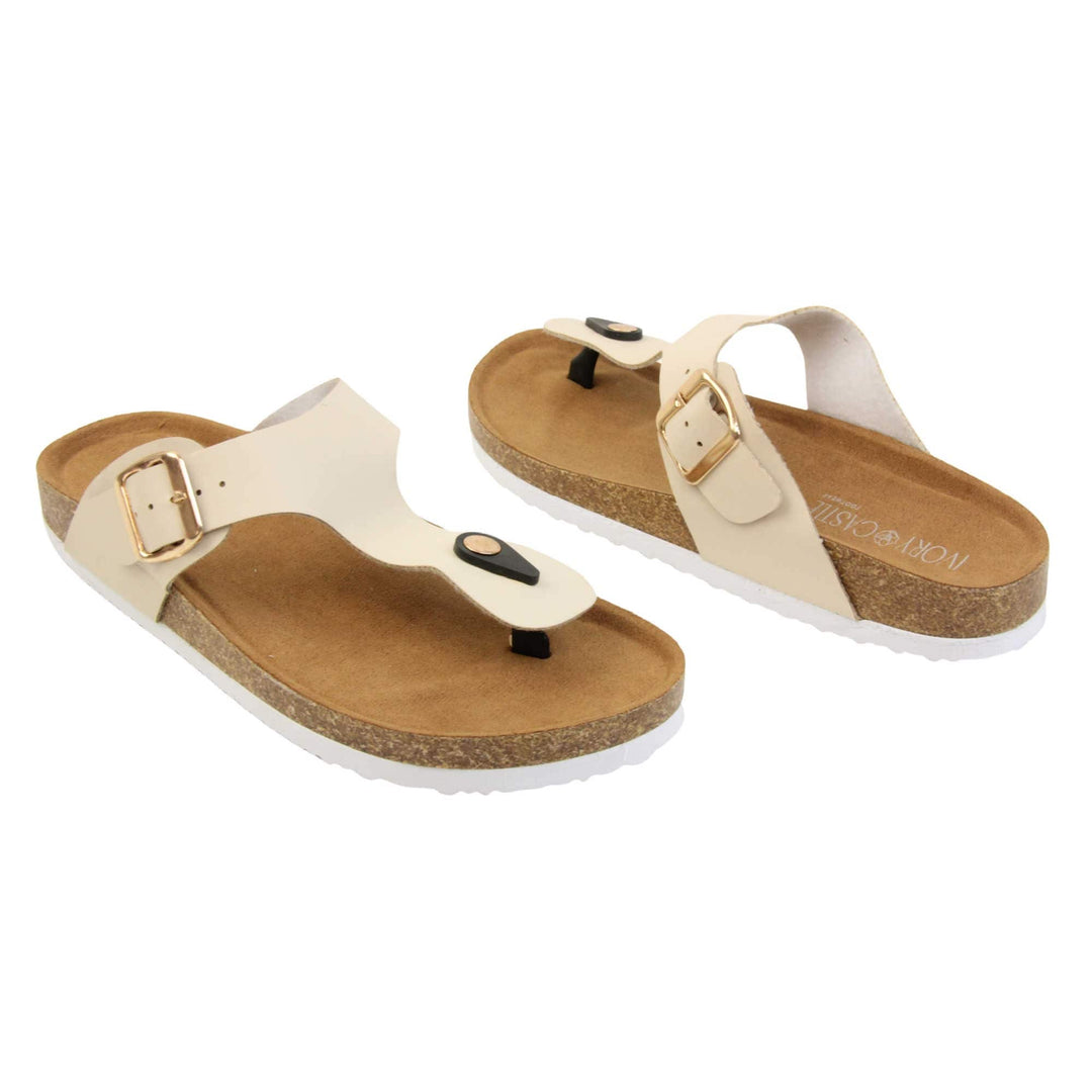Cream flip flops. Cream faux leather strap with toe post to the front and gold buckle to the outside. Soft tan faux suede footbed with cork effect outsole and white sole.  Both feet at an angle facing top to tail.