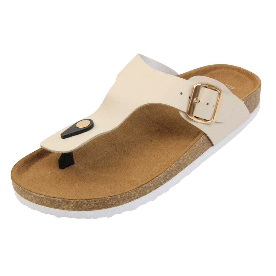 Cream flip flops. Cream faux leather strap with toe post to the front and gold buckle to the outside. Soft tan faux suede footbed with cork effect outsole and white sole. Left foot at an angle.