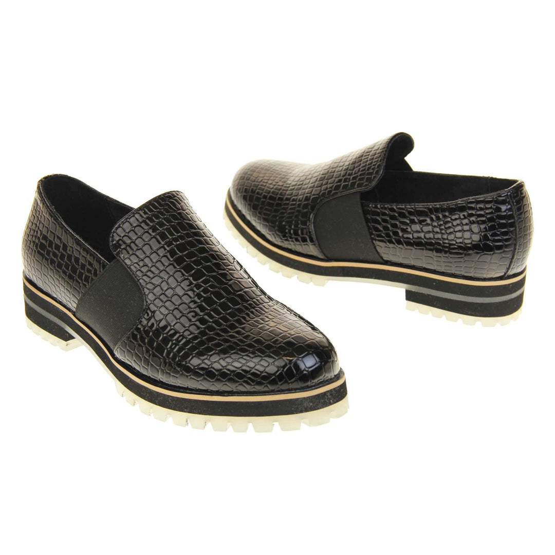 Croc loafers womens. Loafer style shoes with a black faux snakeskin upper. With twin black elasticated side panels. Chunky black and cream sole with slip resistant grip to the bottom. Both feet at an angle facing top to tail.
