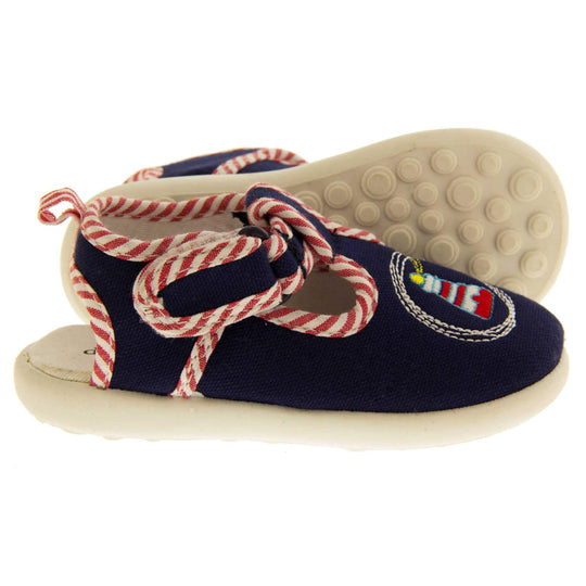 Boys sandals. Navy canvas sandals with cut out heel. White sole with lighthouse detail on the front of the shoes and red and white striped edging. Both shoes from side profile with left foot on its side to show the sole.