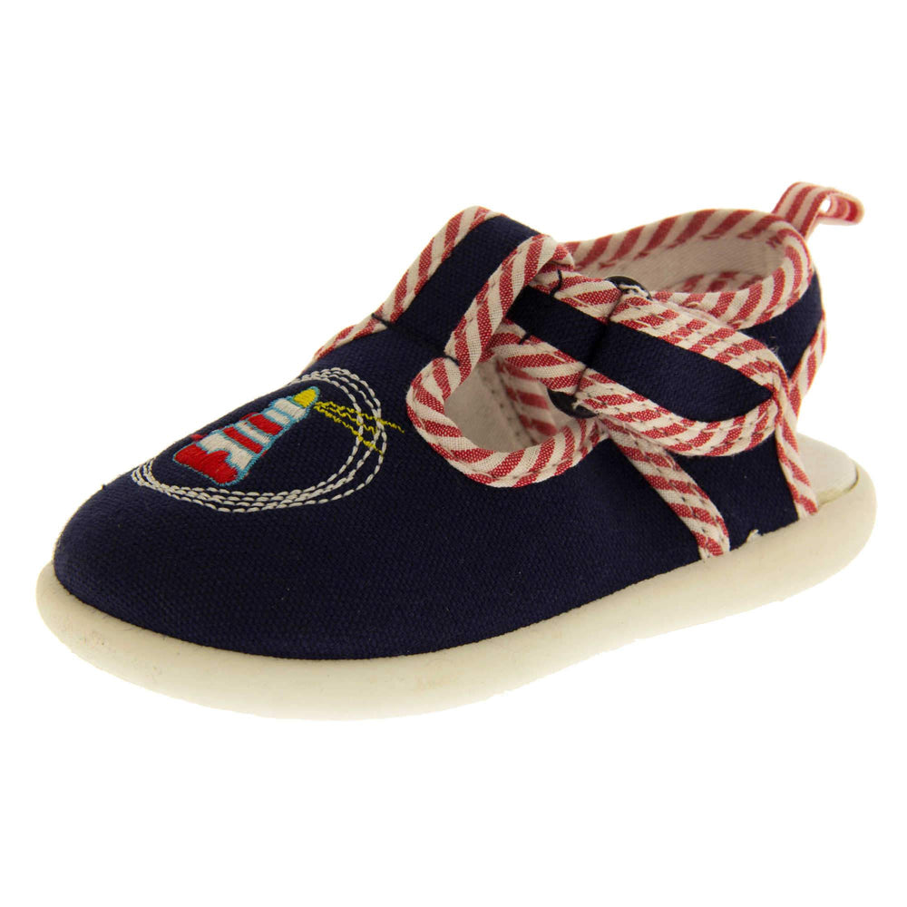 Boys sandals. Navy canvas sandals with cut out heel. White sole with lighthouse detail on the front of the shoes and red and white striped edging. Left foot at angle.