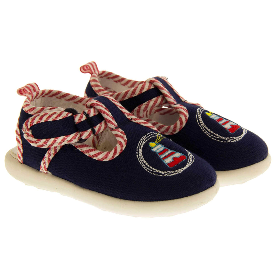 Boys sandals. Navy canvas sandals with cut out heel. White sole with lighthouse detail on the front of the shoes and red and white striped edging. Both shoes next to each other.