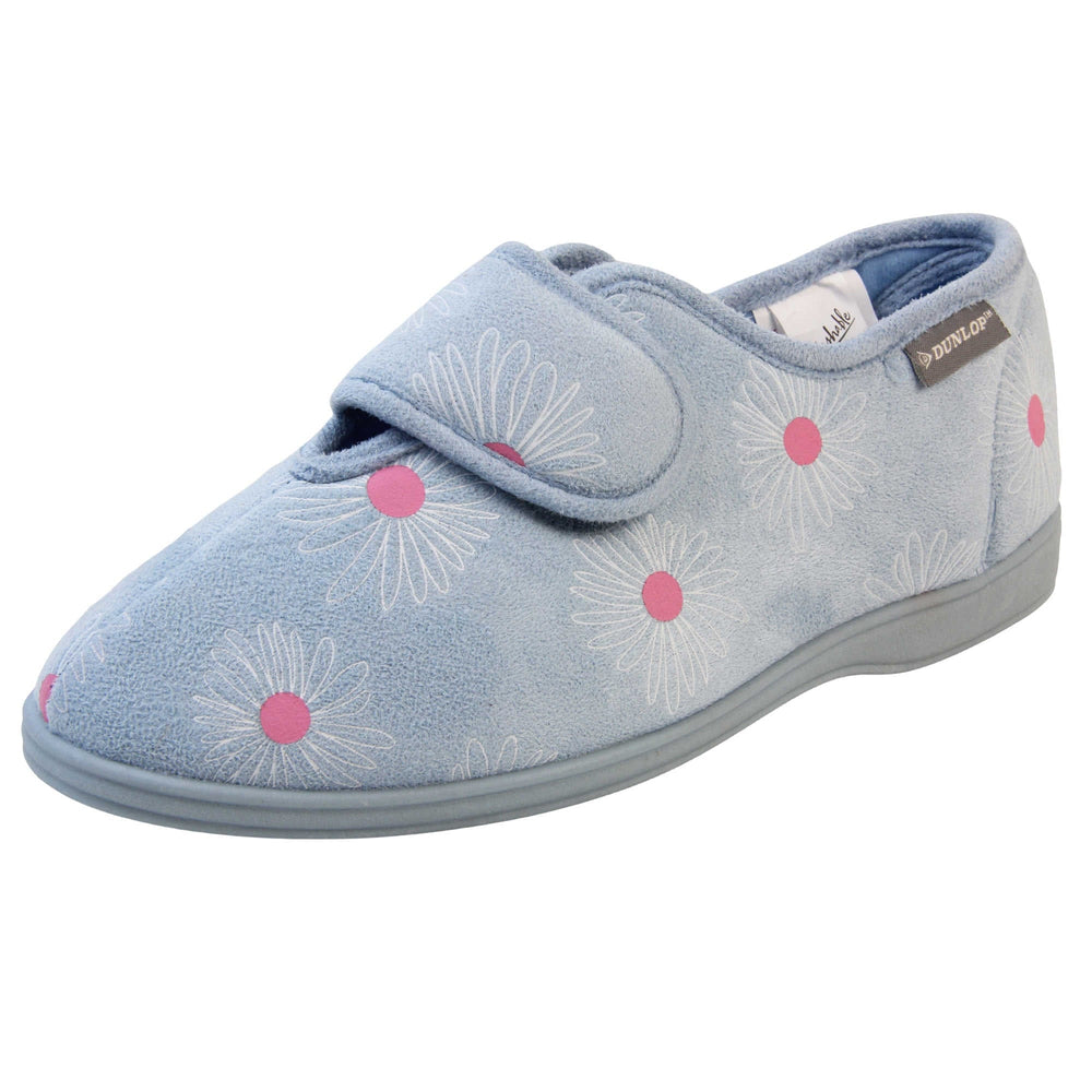 Slippers for swollen feet. Womens full back slipper. With a pale blue upper with white daisy design with bright pink for the middle of the flowers. Touch fasten strap over the top of the foot to adjust the fit. Matching blue textile lining and sole. Left foot at an angle.