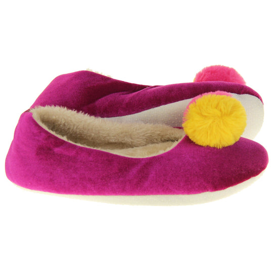 Womens ballet slippers. Ladies slippers in a ballerina style. Fuchsia velvety upper with fluffy yellow and pink pom pom on the top. Cream faux fur lining. Beige textile sole with bumps to the bottom for grip. Both feet from a side profile with the left foot on its side to show the sole.