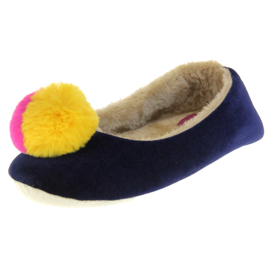 Womens ballerina slippers. Ladies slippers in a ballerina style. Navy blue velvety upper with fluffy yellow and pink pom pom on the top. Cream faux fur lining. Beige textile sole with bumps to the bottom for grip. Left foot at an angle.