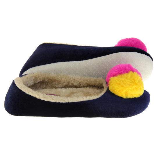 Womens ballerina slippers. Ladies slippers in a ballerina style. Navy blue velvety upper with fluffy yellow and pink pom pom on the top. Cream faux fur lining. Beige textile sole with bumps to the bottom for grip. Both feet from a side profile with the left foot on its side to show the sole.
