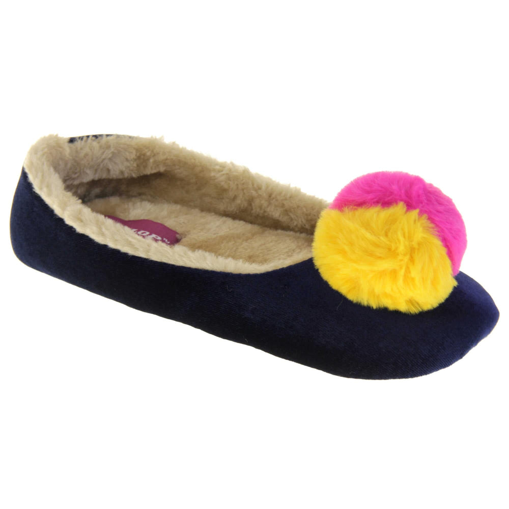 Womens ballerina slippers. Ladies slippers in a ballerina style. Navy blue velvety upper with fluffy yellow and pink pom pom on the top. Cream faux fur lining. Beige textile sole with bumps to the bottom for grip. Right foot at an angle.