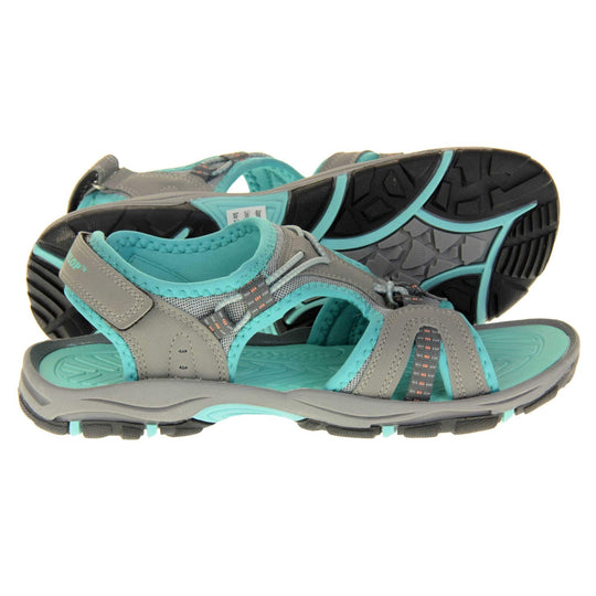 Dunlop womens walking sandals - Light grey faux leather upper with decorative elasticated strap detailing and teal blue trim. Hook and loop touch fastening ankle strap for secure fitting. Turquoise padded insole for extra comfort and a teal, grey and black flexible outsole with good grips for hiking. Right foot side view, left foot outsole visible.
