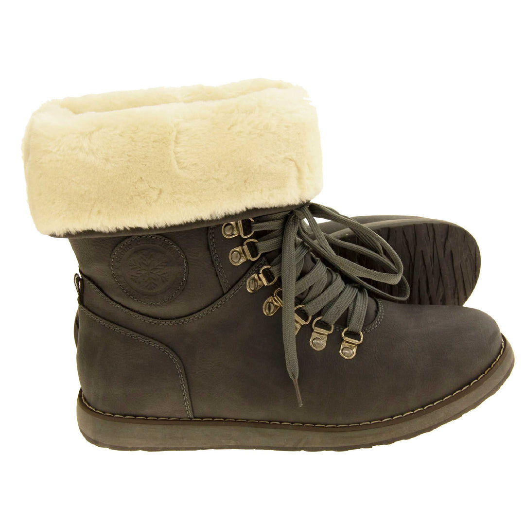 Faux fur lined winter boot. Women's boot in an ankle style with a grey faux suede upper. Pull on design with grey faux laces detail to the front. Cream faux fur lining and collar. Grey sole with grip to the bottom. Both feet from a side profile with the left foot on its side to show the sole.