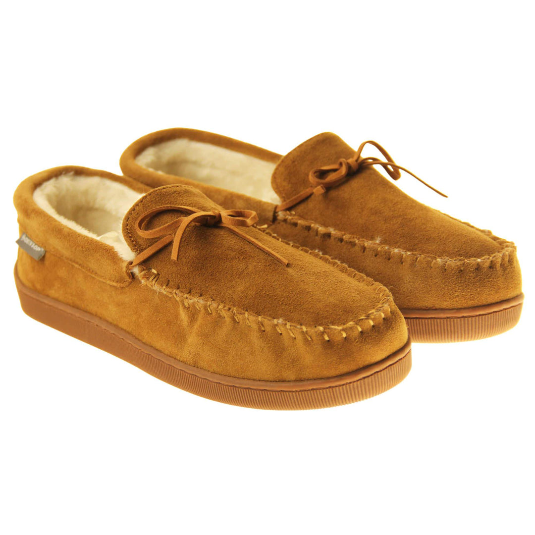 Faux fur moccasins. Closed back slippers in a moccasin style with tan brown suede leather upper and bow. Cream faux fur lining. Thick brown sole. Both feet together at an angle.