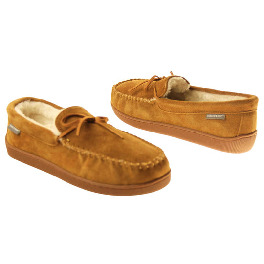 Faux fur moccasins. Closed back slippers in a moccasin style with tan brown suede leather upper and bow. Cream faux fur lining. Thick brown sole. Both shoes at an angle spaced about an inch apart, facing top to tail at an angle.
