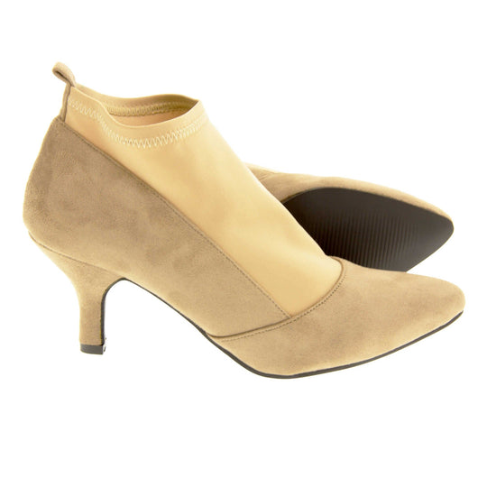 Faux suede ankle boots. Womens taupe faux suede ankle boot with a stretchy nude fabric panel to the front and around the top of the ankle. Small faux suede loop to the back for pulling onto your feet. Small taupe faux suede heel and black sole. Both feet from a side profile with the left foot on its side behind the the right foot to show the sole.