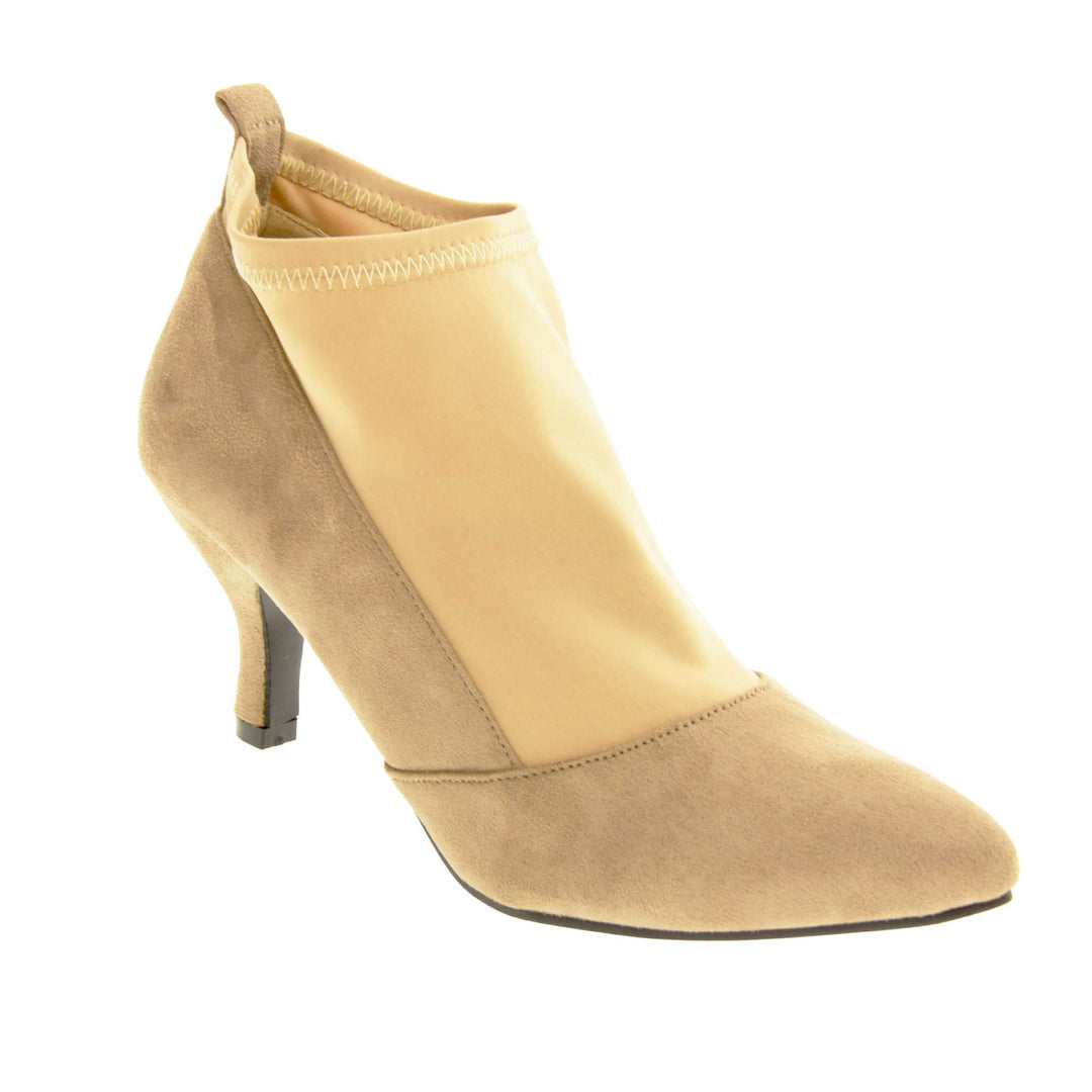 Faux suede ankle boots. Womens taupe faux suede ankle boot with a stretchy nude fabric panel to the front and around the top of the ankle. Small faux suede loop to the back for pulling onto your feet. Small taupe faux suede heel and black sole. Right foot at an angle.