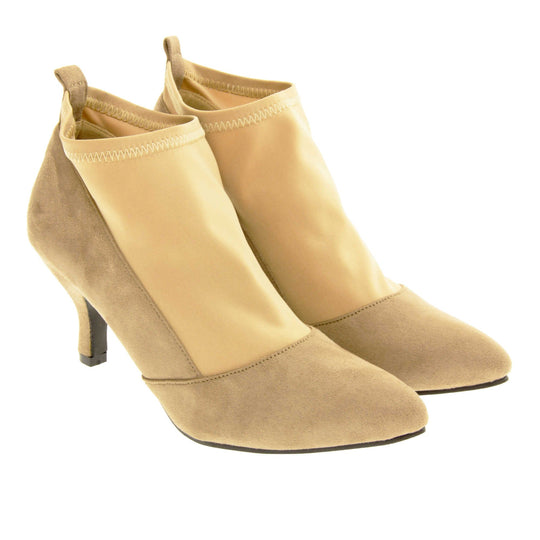 Faux suede ankle boots. Womens taupe faux suede ankle boot with a stretchy nude fabric panel to the front and around the top of the ankle. Small faux suede loop to the back for pulling onto your feet. Small taupe faux suede heel and black sole. Both feet together at a slight angle.
