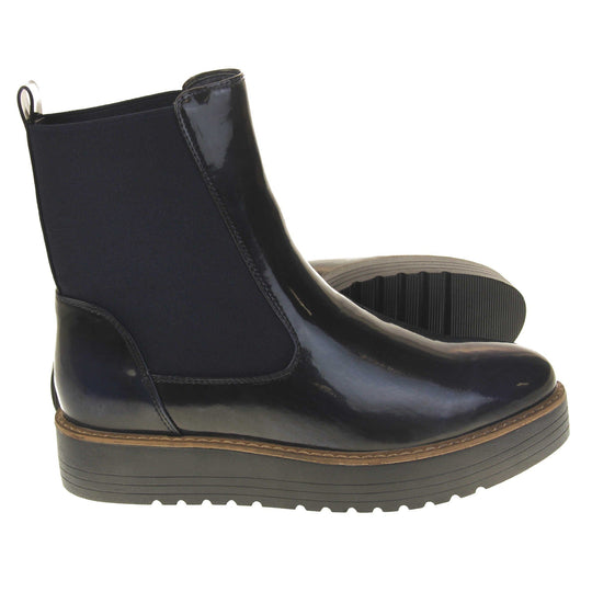 Fleece lined boots women's. Faux leather, tall Chelsea boot style with a black upper. Black elasticated panels at the ankles and a black loop at the heel to help pull them on. Black coloured low platform sole. Both feet from a side profile with the left foot on its side to show the sole.