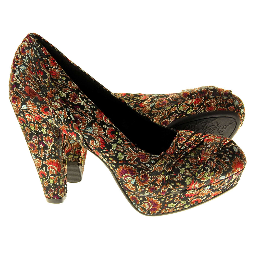 Floral block heels. Womens high heels with a floral textile upper. Ruched detailing to the front. Black textile lining with a red circle on the insole with black Rocket Dog logo. Small platform on the front of the outsole with a chunky block heel to the back covered in the same textile as the upper. Black sole to the bottom. Both feet from a side profile with the left foot on its side behind the the right foot to show the sole.