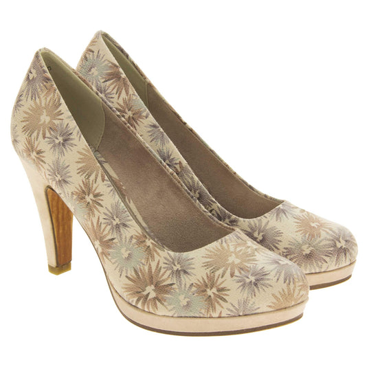 Floral heels. Womens court shoes with a cream upper with faded floral multi coloured pattern. Matching insole with Marco Tozzi branding. Taupe faux suede lining. Small cream platform and mid stiletto heel. Brown sole. Both feet together at a slight angle.