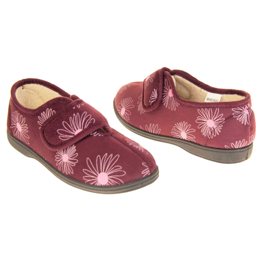 Floral slippers. Womens full back slipper. Burgundy upper with white daisy design and bright pink for the middle of the flowers. Touch fasten strap over the top of the foot to adjust the fit. Cream fleece lining and firm black sole. Both feet at an angle, facing top to tail.