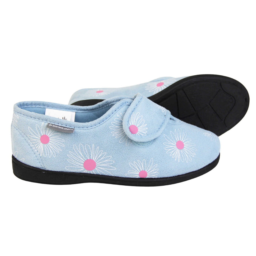 Flower slippers. Womens full back slipper. Pale blue upper with white daisy design and bright pink for the middle of the flowers. Touch fasten strap over the top of the foot to adjust the fit. Matching blue textile lining and firm black sole.  Both feet from a side profile with the left foot on its side behind the the right foot to show the sole.