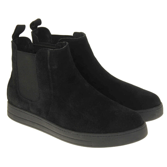 Fur lined ankle boots women's. Chelsea style boot with a black suede upper. Black elasticated panels at the ankles and black faux fur lining. A loop at the heel to help pull them on. Black outsole.  Both feet together from an angle.