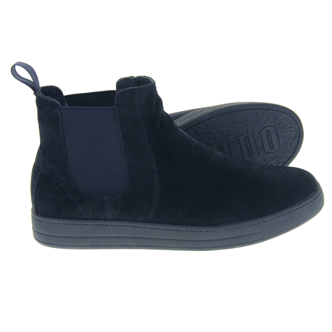 Fur lined Chelsea boots. Women's ankle boot with a navy blue suede upper. Navy elasticated panels at the ankles and navy faux fur lining. A navy loop at the heel to help pull them on. Black outsole. Both feet from a side profile with the left foot on its side to show the sole.