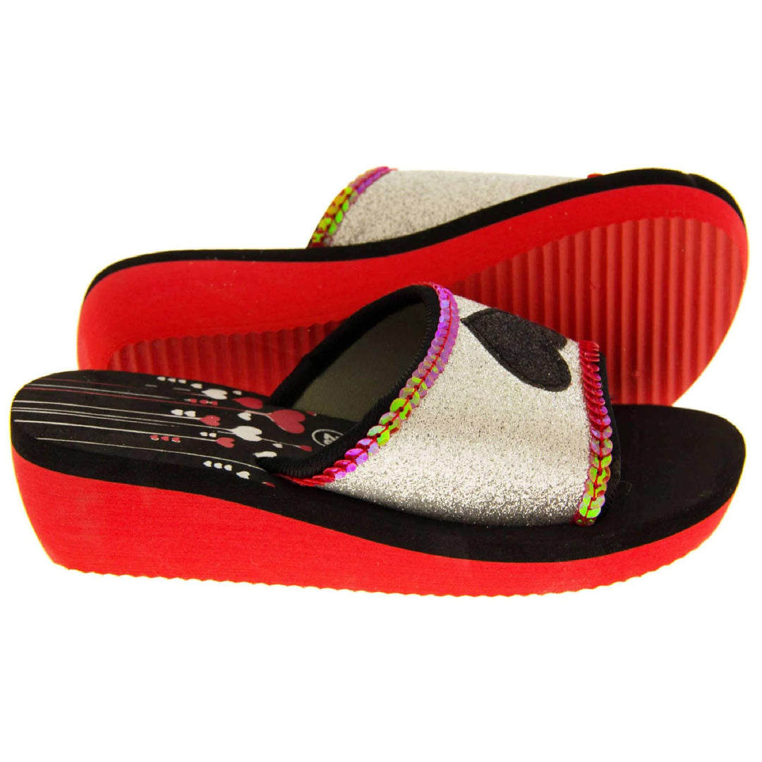 Foam wedge sandals for girls. Red bottom half of the sole with ridges for grip, black top half with red and white heart and line design to the heel of the insole. Silver glitter full strap with black glitter heart in the middle and pink sequins along the edges. Both feet from side profile with left foot on its side to show the sole.