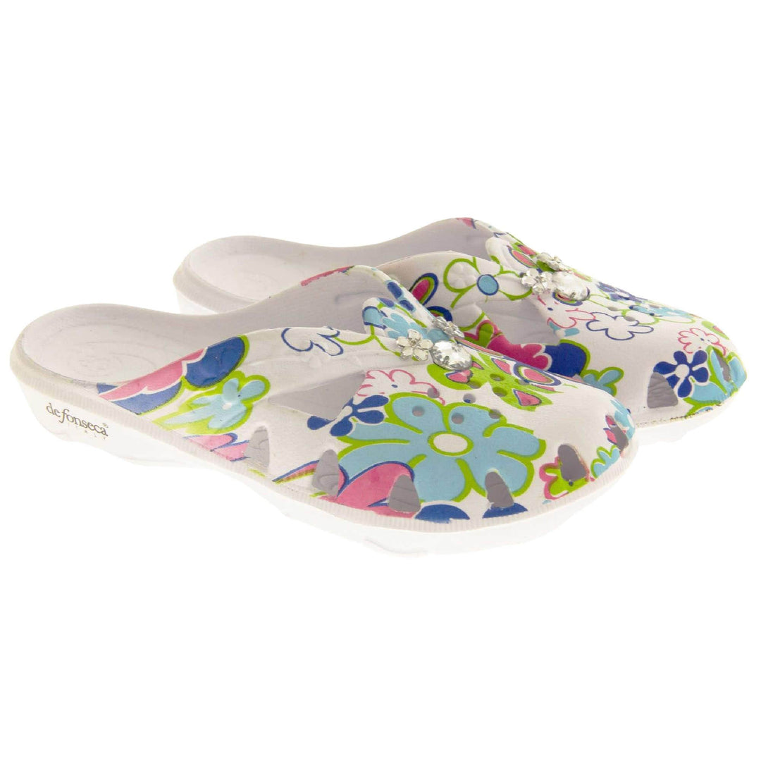 Girls Clogs. White synthetic clogs in a mule style. Cut out holes around the toes and the upper. Bright, fun floral print on the upper with diamante detailing to the centre. Matching white sole. Both shoes next to each other at a slight angle.