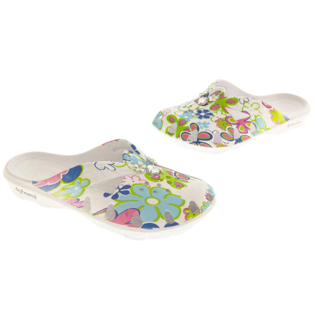 Girls Clogs. White synthetic clogs in a mule style. Cut out holes around the toes and the upper. Bright, fun floral print on the upper with diamante detailing to the centre. Matching white sole. Both shoes in an L shape at a slight angle.