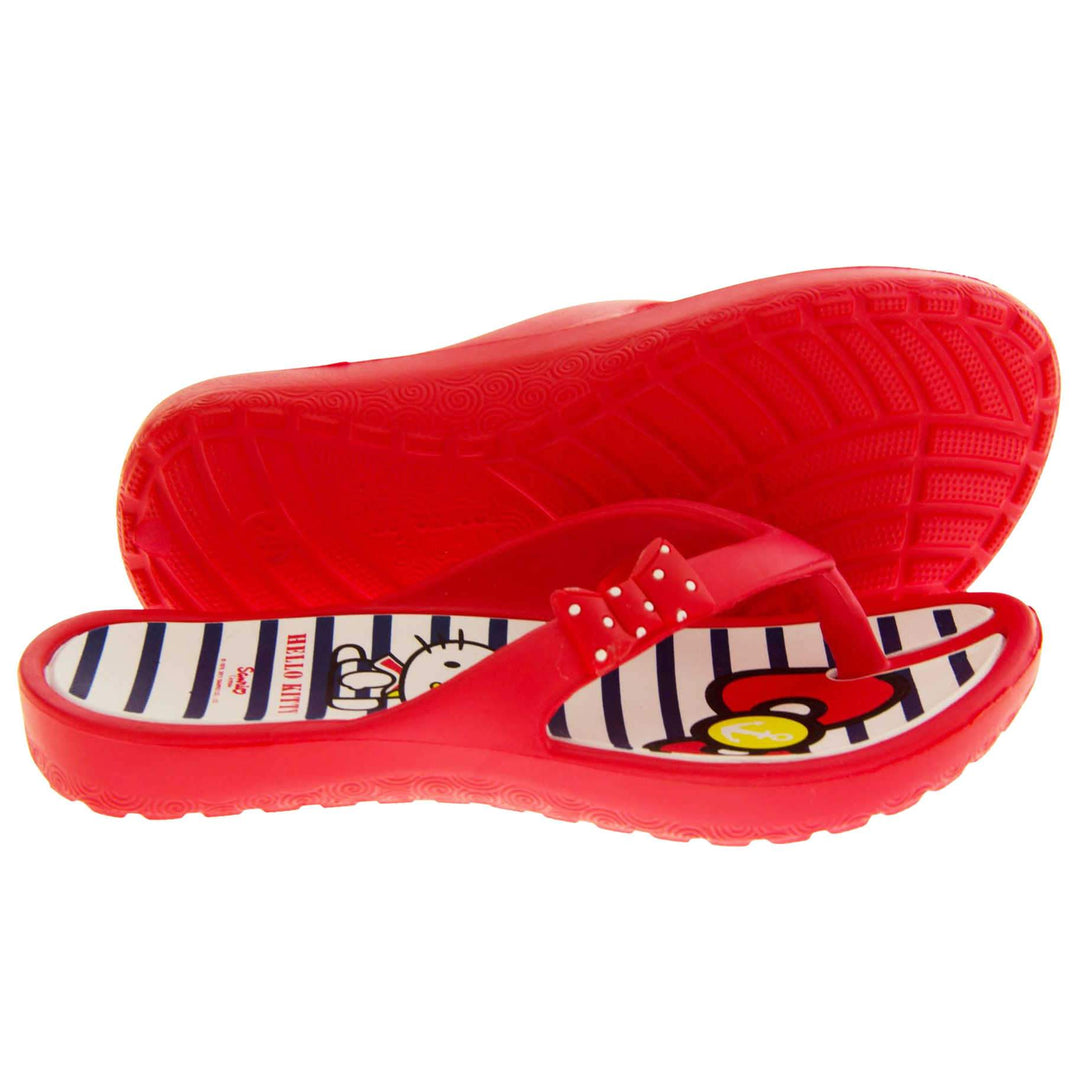 Girls flip flop. Hello Kitty flip flop with red sole and straps in a toe-post design with small red bow with white spots on. White and navy striped insole with Hello Kitty design on. Both shoes from a size profile with the left foot on its side to show the sole.