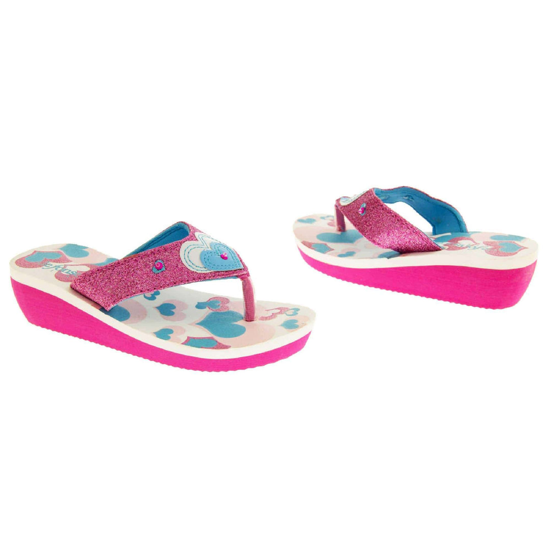 Girls glitter sandals. Foam wedge sandals for girls. Pink bottom half of the sole with ridges for grip, white top half with heart designs in pale pink, bright pink and teal. Bright pink glitter strap with toe-post. With cream and teal heart detail to the strap and pink diamantes.  Both feet at an angle facing top to tail.