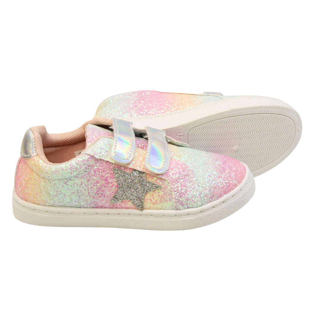 Girls glitter trainers. Kids trainers with a ombre rainbow upper done in glitter. With two silver holographic touch fasten straps. A silver glitter heart detail to the outside of the shoe in the middle of the foot. Pale pink textile lining and chunky white sole.  Both feet from a side profile with the left foot on its side behind the the right foot to show the sole.