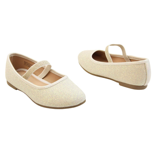 Girls party shoes. Ballerina style shoes with ivory glitter uppers. With a gold glitter elasticated over the foot strap. Cream faux leather collar and beige lining. Dark brown sole with very slight heel. Both feet at an angle facing top to tail.