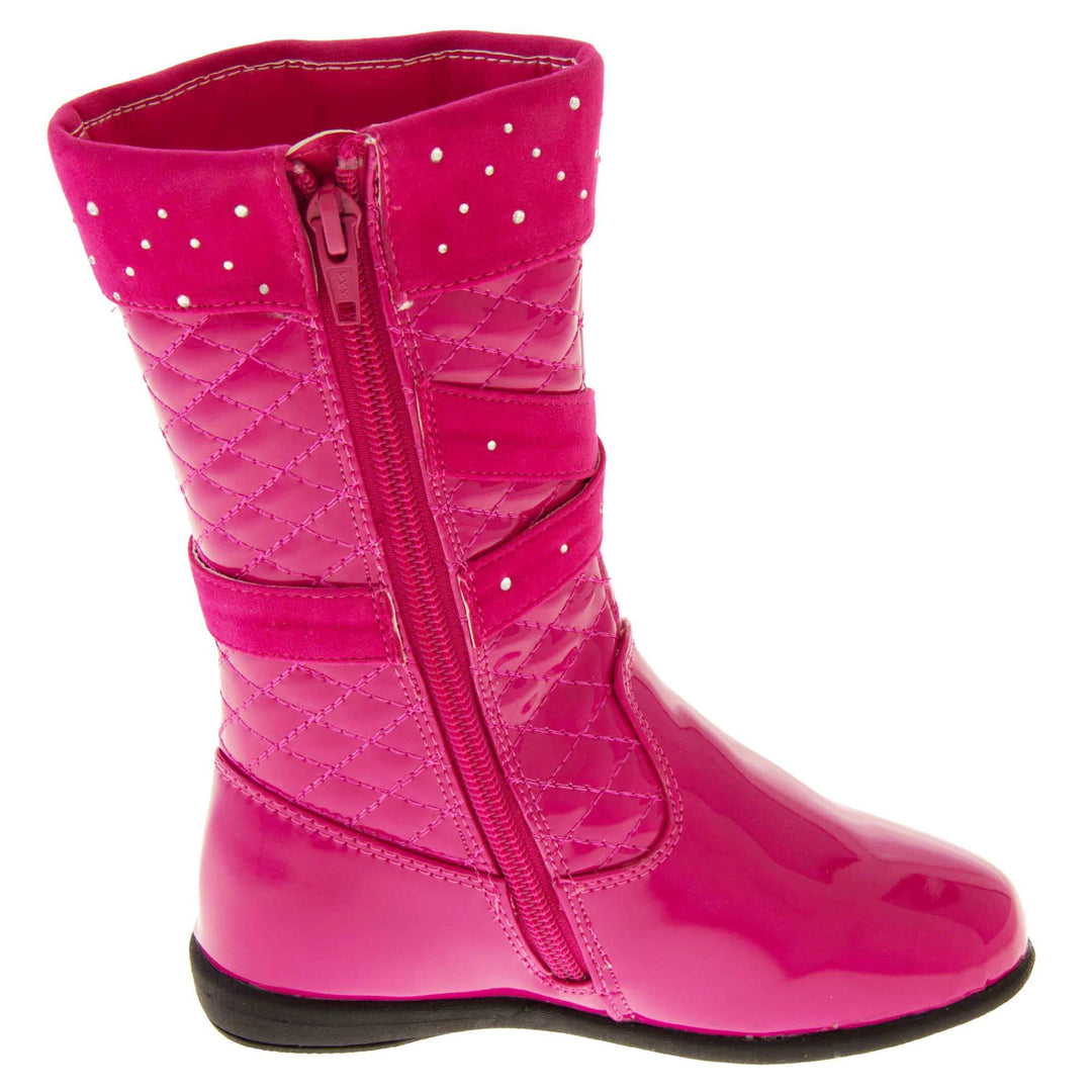 Girls pink boots. Fuchsia patent leather effect uppers with ankle upwards being a quilted style. With faux suede cuff and straps that both have diamantes on. Diamante buckle on the straps. Zip fastening to the inside leg. Black synthetic sole. Side profile of left foot to show the zip on the inside leg.