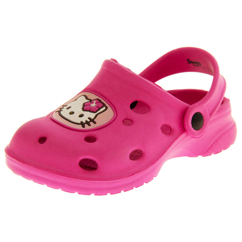 Girls Sandals Pink. Fuchsia pink synthetic clog sandals with holes in the upper. Hello Kitty face in a pale pink circle to the front. Pink strap with black studs to attach to the back of the shoe. The strap can be worn around the back of the heel or over the top of the shoe in a mule. Pink sole with slight heel to the back. Left foot at an angle