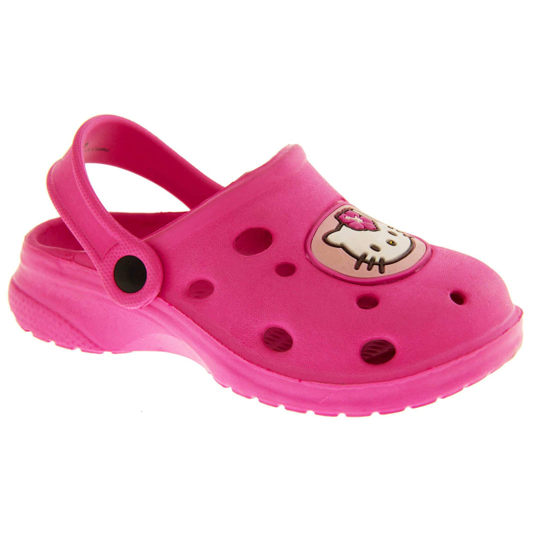 Girls Sandals Pink. Fuchsia pink synthetic clog sandals with holes in the upper. Hello Kitty face in a pale pink circle to the front. Pink strap with black studs to attach to the back of the shoe. The strap can be worn around the back of the heel or over the top of the shoe in a mule. Pink sole with slight heel to the back. Right foot at an angle